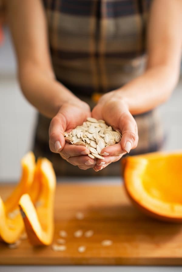 hands holding pumpkin seeds with pumpkin in foreground