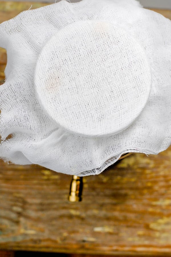 Cheesecloth covering the top of a jar of apple cider vinegar as part of how to make vinegar