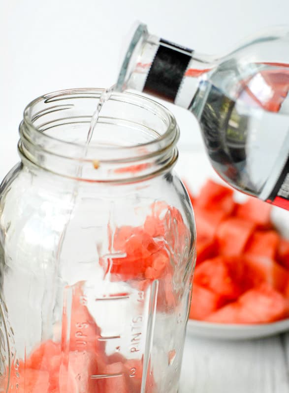 Watermelon chunks in Mason jar and tequila pouring in