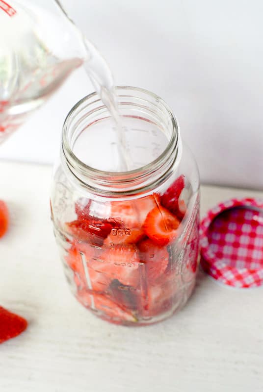 Pouring Vodka into a jar of strawberries