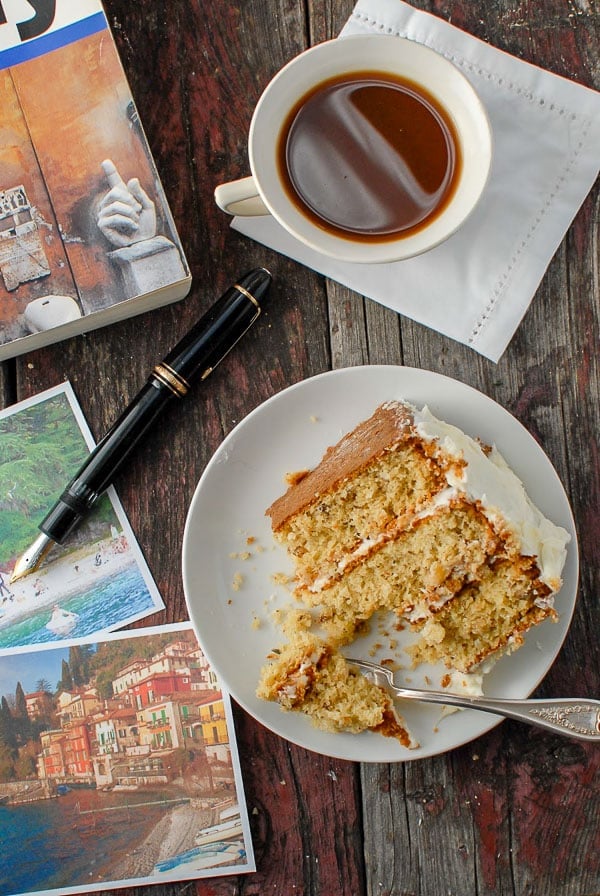 Partial slice of Italian Cream Cake with cup of coffee and travel book