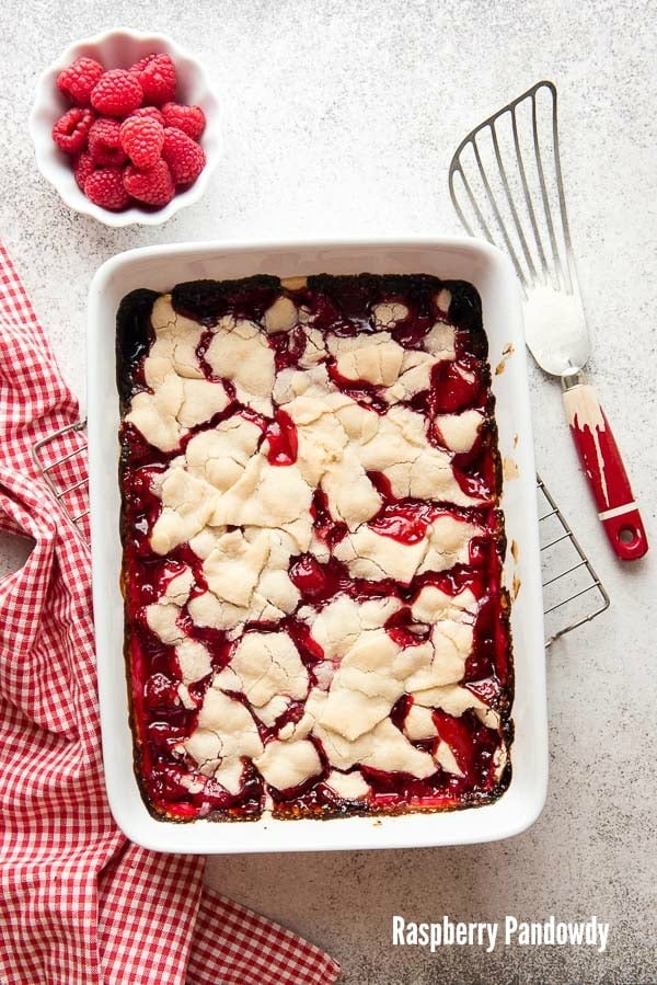 Freshly baked Raspberry Pandowdy dessert in a white baking dish with a bowl of fresh raspberries