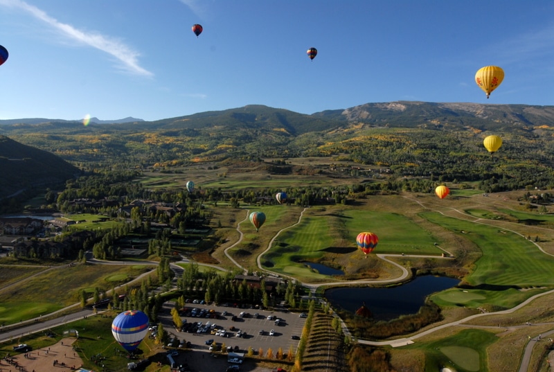 A group of people flying balloons on a grassy hill