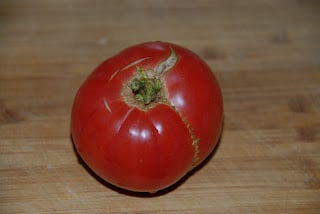 A tomato sitting on top of a wooden cutting board