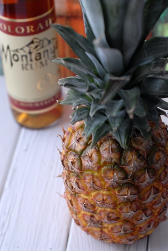 A pineapple sitting on a table with bottle of rum