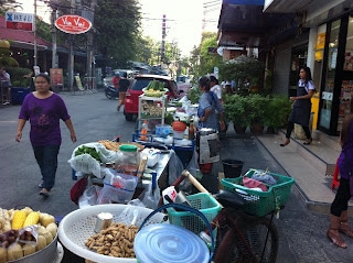 A group of people sitting at a table with food, with Street and Vendor
