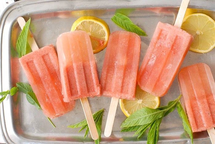 Refreshing boozy Costa Rican Watermelon Mojito Popsicles, frozen cocktail popsicles with lemon, mint on vintage white boards.
