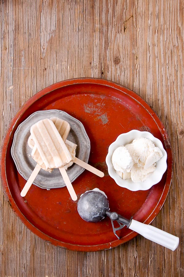 Three Root Beer Float Popsicles with wooden sticks, on a pewter plate with white bowl of vanilla ice cream