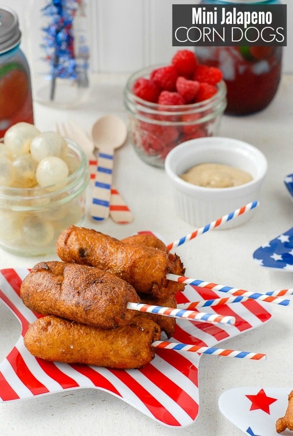 Mini Jalapeno Corn Dogs iwth patriotic sticks on a striped star plate with food in background