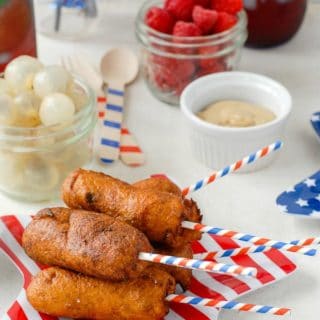 Mini Jalapeno Corn Dogs iwth patriotic sticks on a striped star plate with food in background