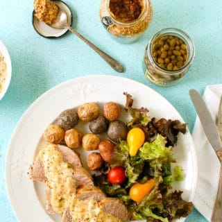 Quick and tasty Pork Tenderloin with Mustard Caper Cream Sauce on a vintage white ironstone plate and blue plaster background