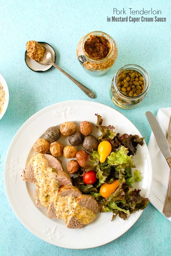 Quick and tasty Pork Tenderloin with Mustard Caper Cream Sauce on a vintage white ironstone plate and blue plaster background