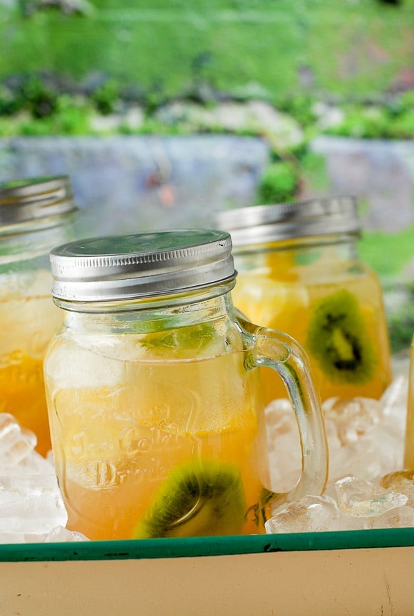 Chilled Tropical Fruit Sangria with kiwi and pineapple slices in Mason jar mugs with silver lids
