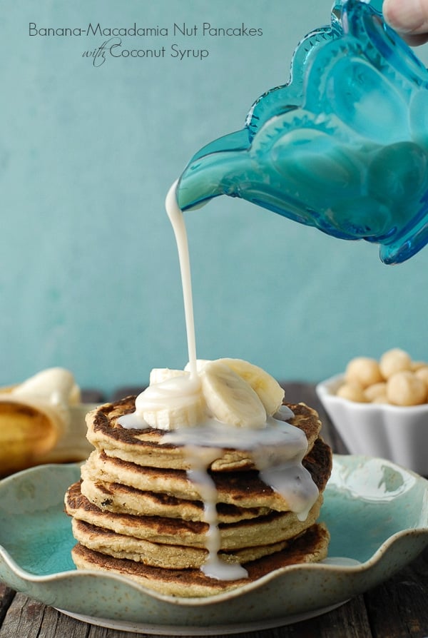 coconut syrup being poured over a stack of Banana-Macadamia Nut Pancakes