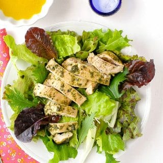 Quick, juicy chicken breasts topped with homemade tarragon pesto served on dressed mixed green salad on a white plate