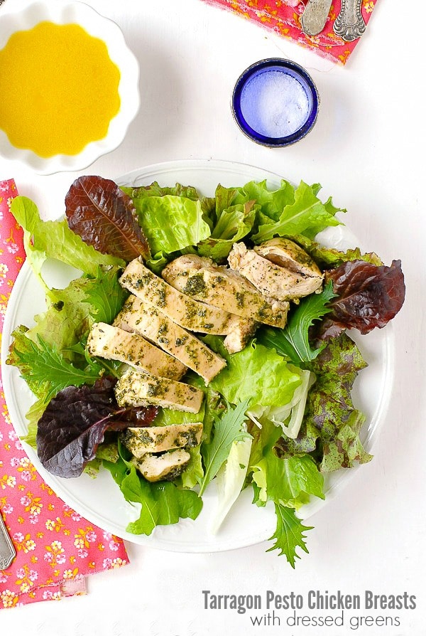 Quick, juicy chicken breasts topped with homemade tarragon pesto served on dressed mixed green salad on a white plate 