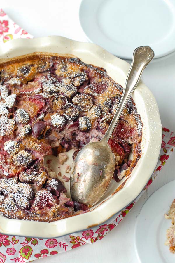 Freshly baked Cherry Strawberry Claufoutis (crustless custard fruit dessert) in a ruffled deep dish pie pan 