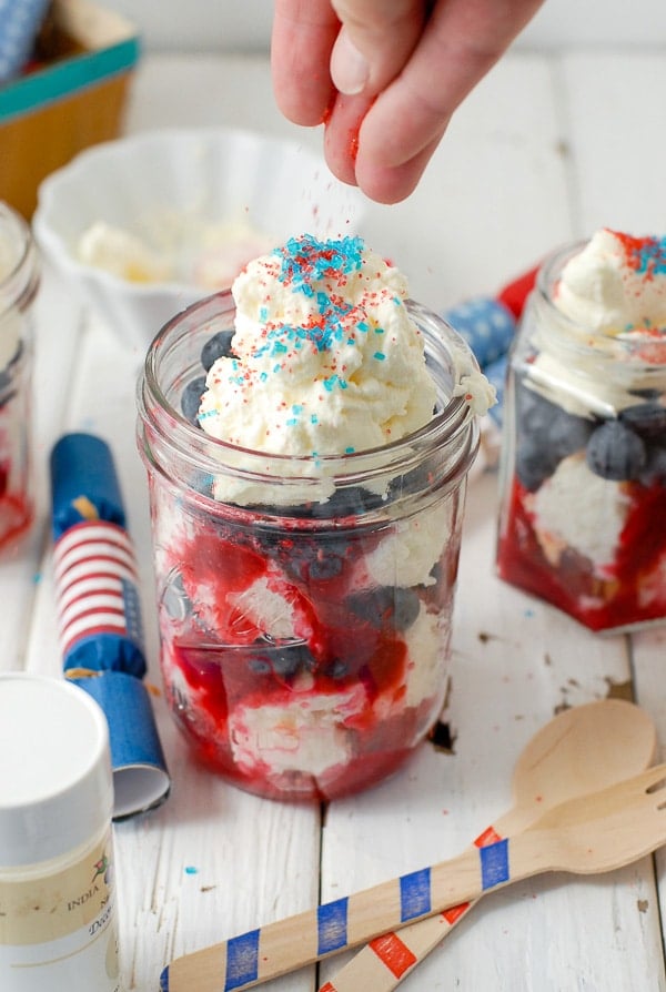 Sprinkling sparkling sugar onto the top of a red white and blue trifles in a jar