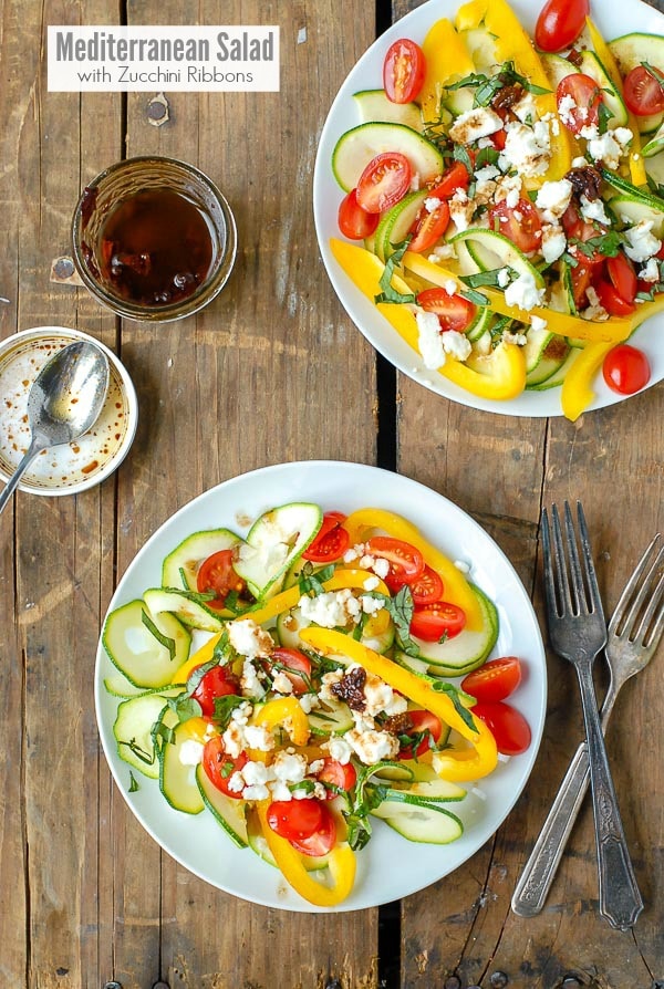 Two white plates of Meditteranean Salad with Zucchini Ribbons and Sun Dried Tomato Balsamic Vinaigrette