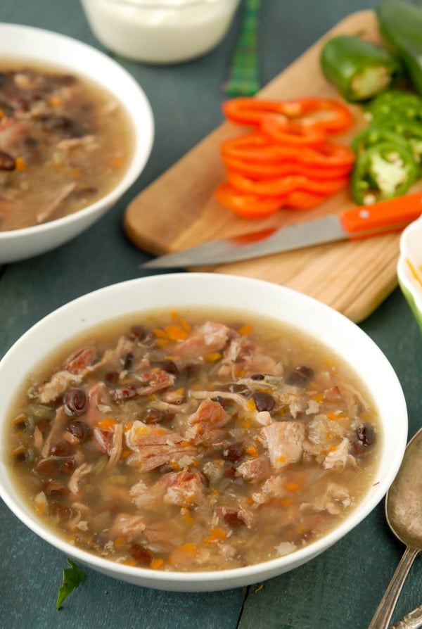 Close up of steamy slow cooker black bean and hambone soup with sliced red peppers in the background