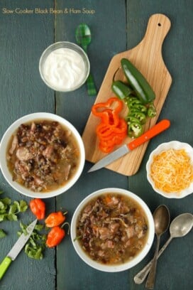Two white bowls of slow cooker black bean and hambone soup with cumin with freshly cut peppers