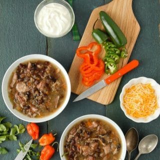 Two white bowls of slow cooker black bean and hambone soup with cumin with freshly cut peppers