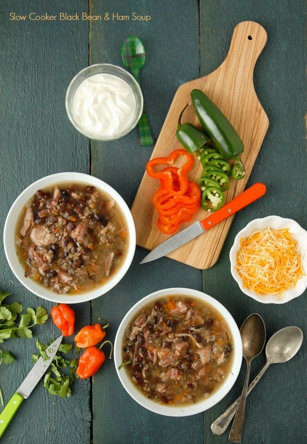 Two white bowls of slow cooker black bean and hambone soup with cumin with freshly cut peppers