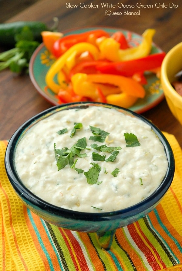 Slow Cooker White Queso Green Chile Dip in blue glass bowl with sliced colorful sweet peppers