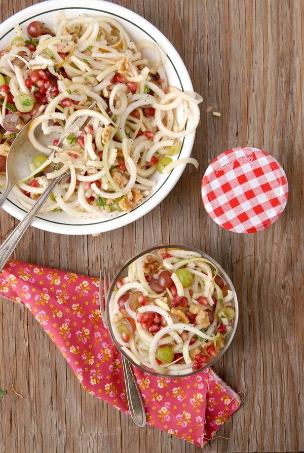 A serving bowl and individual serving of Spiralized Apple and Pears Pomegranate Slaw with Honey-Poppy Seed Dressing