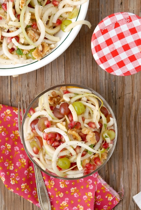 Glass bowl of spiralized Apple and Pears Pomegranate Slaw with Honey-Poppy Seed Dressing from above with flower napkin