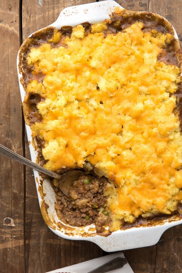 Savory Traditional Cottage Pie in white baking dish with scoop removed showing ground meat with vintage serving spoon