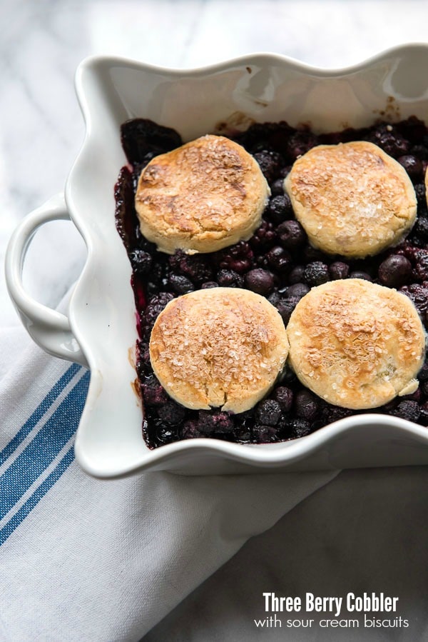 Three Berry Cobbler with Sour Cream Biscuits in a white ruffle-edged baking dish