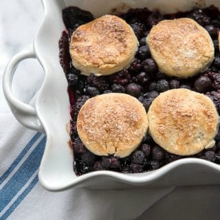 Three Berry Cobbler with Sour Cream Biscuits in a white ruffle-edged baking dish