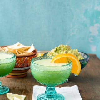 Two blue glasses of Honeydew Melon Margaritas with salted rims and orange slices