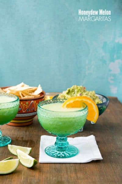 Two blue glasses of Honeydew Melon Margaritas with salted rims and orange slices