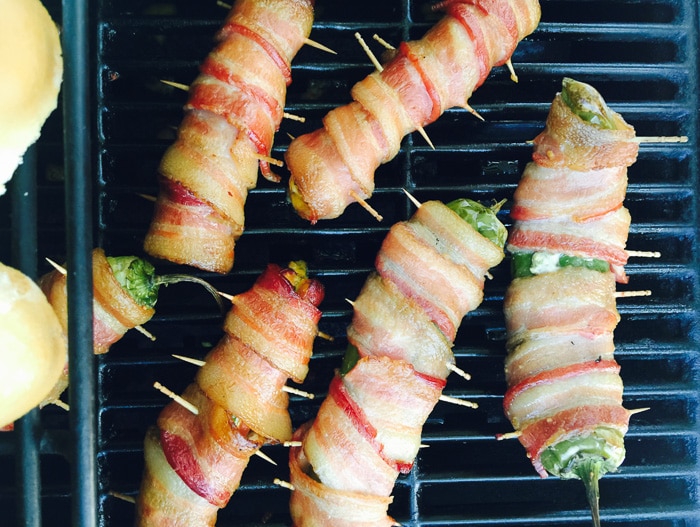 Mesquite-smoked Jalapeno Cheese Bacon-Wrapped Hot Dogs and Peppers on grill