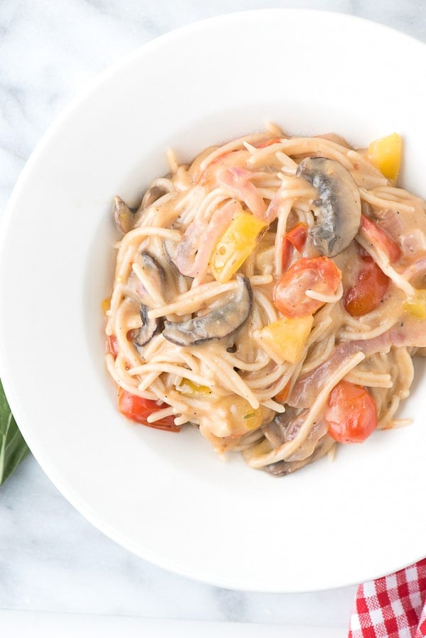 A bowl of pasta sits on a plate, with Tomato and Basil