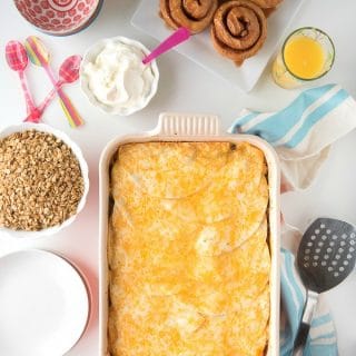 Mexican Breakfast Chicken Tortilla Lasagna Casserole on a table top next to toppings and a plate of cinnamon rolls