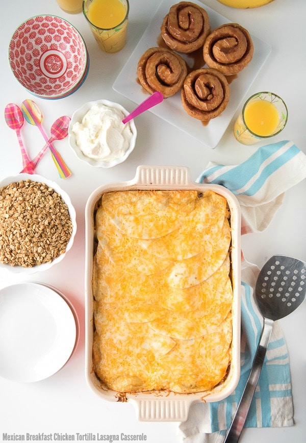 Mexican Breakfast Chicken Tortilla Lasagna Casserole on a table top next to toppings and a plate of cinnamon rolls