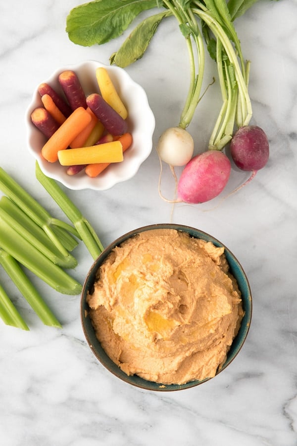 Sriracha Hummus in a bowl with a side of raw vegetables for dipping