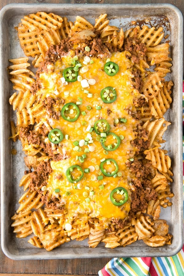 overhead image of a sheet pan with Texas-Inspired Chili Cheese Fries, garnished with fresh jalapeno slices and scallions