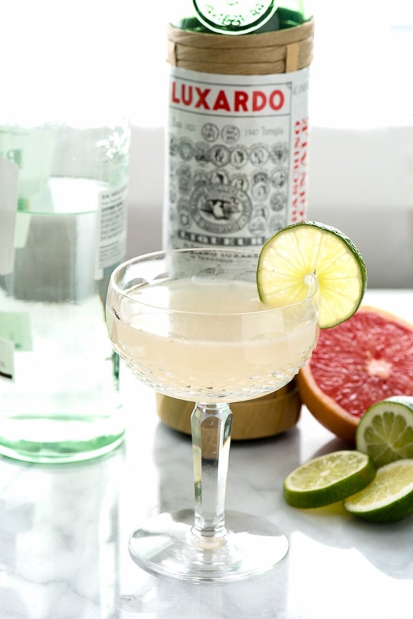 The Hemingway Daiquiri cocktail next to a bottle of Luxardo and fresh citrus fruits