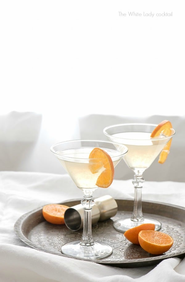 Two The White Lady Cocktails in martini glasses with orange slices on an antique bronze tray