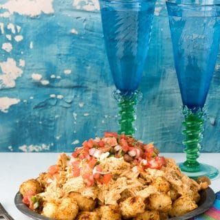 A metal plate of Green Chile Chicken Totchos with blue goblets behind