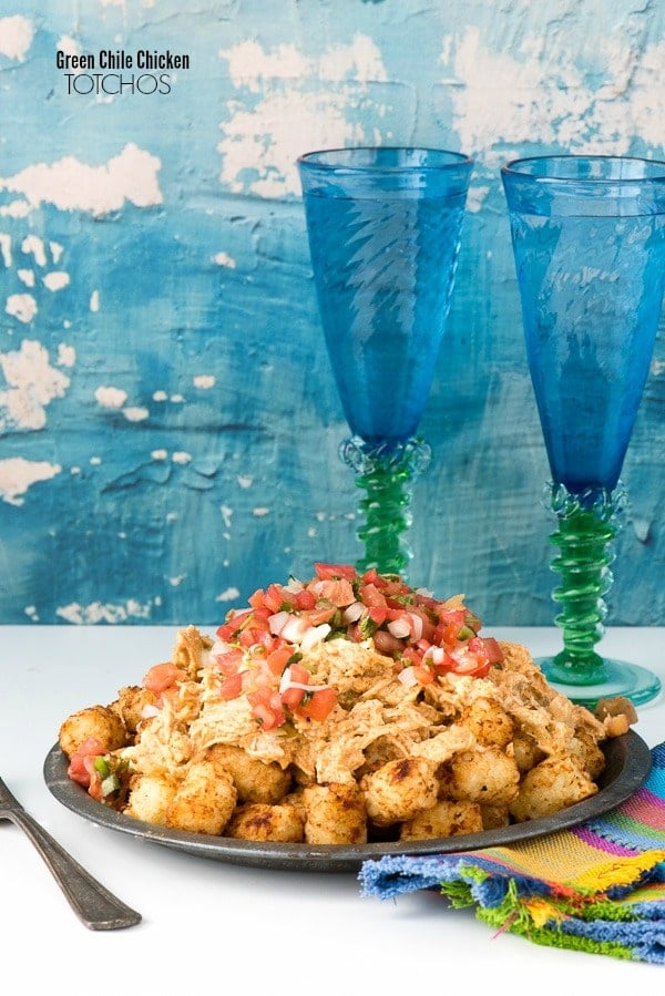A metal plate of Green Chile Chicken Totchos with blue goblets behind