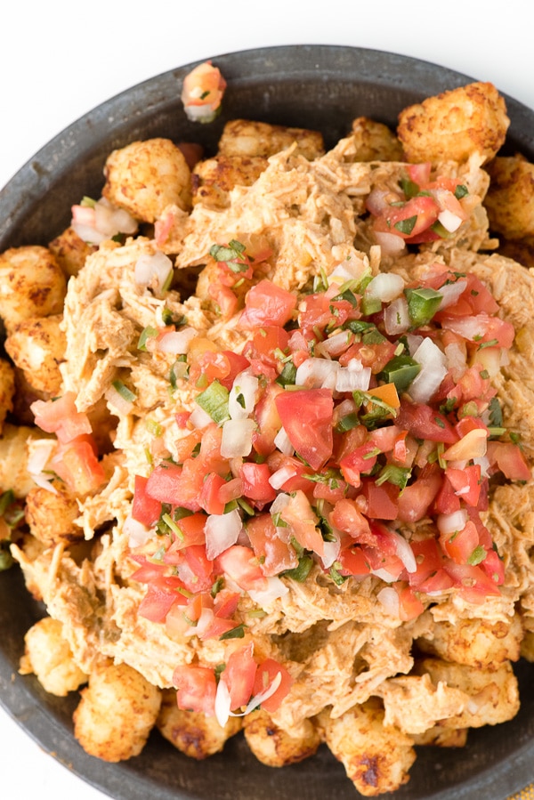Overhead view of a heaping plate of Green Chile Chicken Totchos with pico de gallo salsa