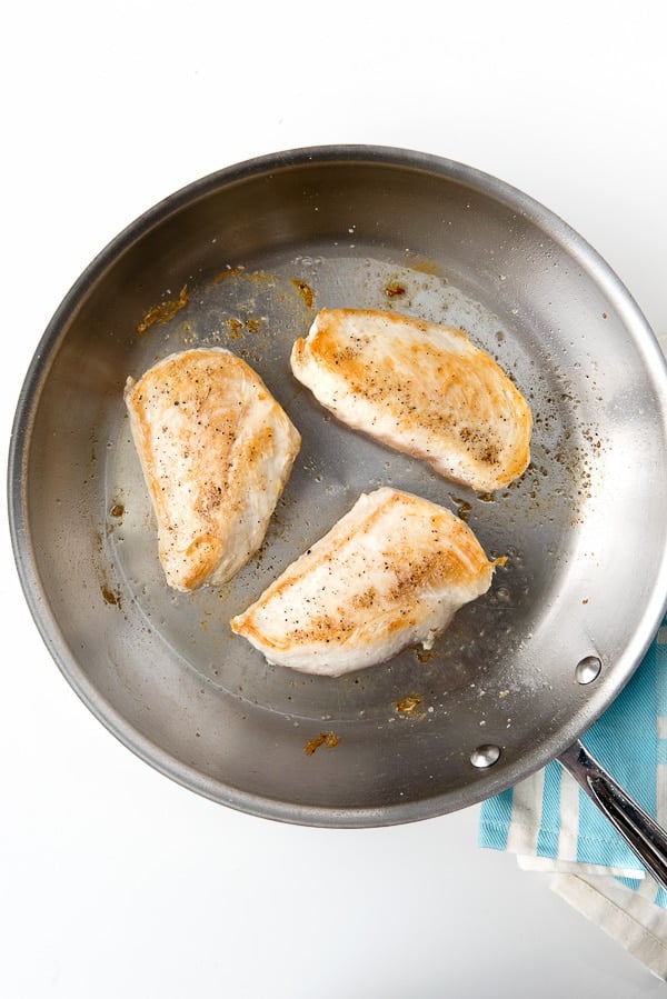 large silver skillet with browned boneless chicken breasts