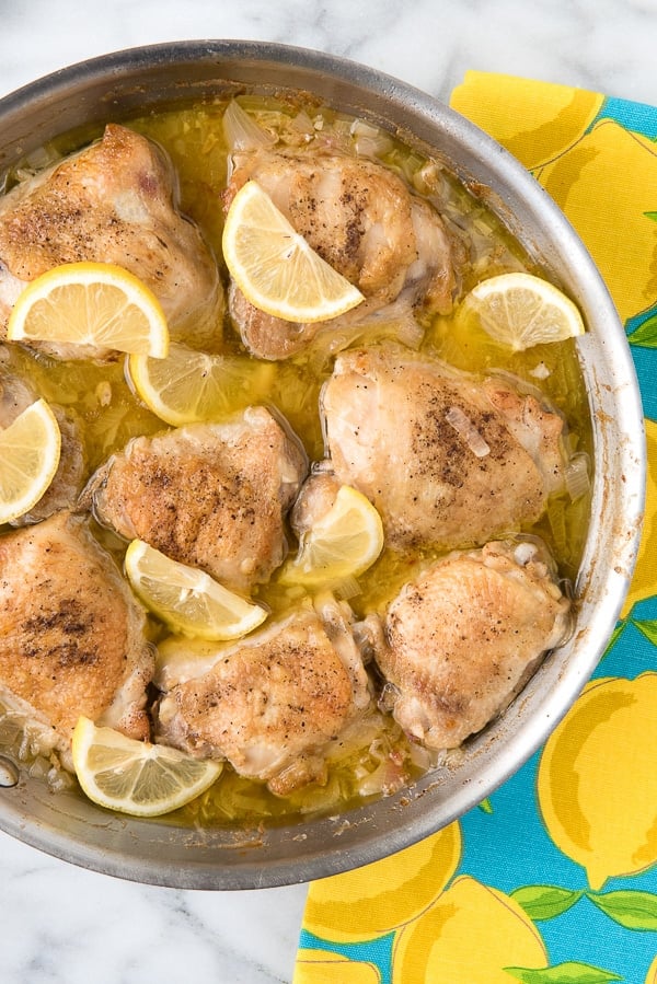 A full silver skillet of Irresistible Lemon-Garlic Braised Chicken Thighs and a blue towel