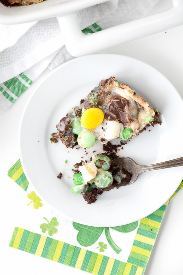 One serving of mint chocolate Leprechaun Bait Bars on a white dessert plate with a fork. A St. Patrick\'s Day themed napkin sits underneath