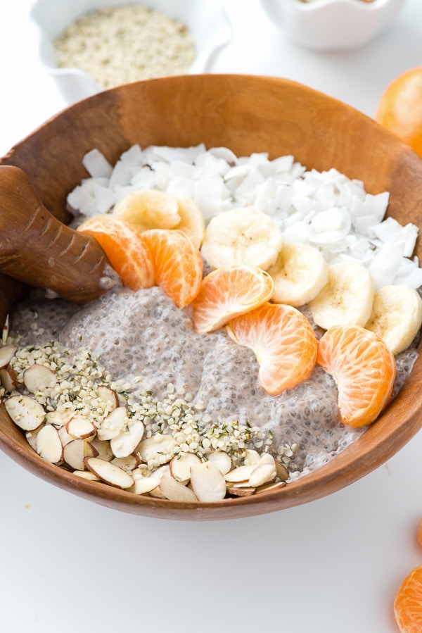 A Roasted Banana Chia Pudding Breakfast Bowl with layers of coconut, banana slices, orange segments, chia seeds and slivered almonds